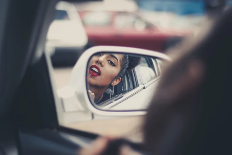 Person doing makeup in car mirror